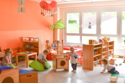 Krippenbereich der Kita Kinderland, Kleinkinder spielen in bunter, altersgerechter Umgebung mit Holzmöbeln, orangefarbene Wand und große Fensterfront im Hintergrund