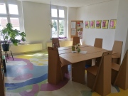 Einrichtung Gemeinschaftsraum bunt bemalter Boden Möbel aus Pappe Pinwand im Hintergrund an den Wänden Bilder der Projektteilnehmer