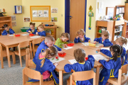 Kreativangebot der Kita Kinderland, Kinder sitzen am Tisch mit blauen Malschürzen und arbeiten mit Stempelkissen