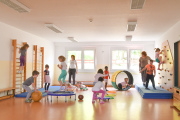 Sportraum der Kita Kinderland, Kinder spielen mit Trampolin, Kletterwand, Reifen, Medizinbällen und Rollwagen