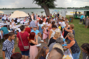 Kuchenbuffet im Seepark, an dem die Gäste schlange stehen und im Hintergrund gedeckte Tische, der See mit Badesteg, Palmen und karibische Sonnenschirme als Deko