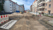 links und rechts Wohnblöcke, an Straßenrändern Baumaterial und Absperrungen, in der Mitte der Straße Sand und Baufahrzeuge