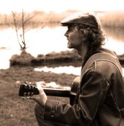 Jörg Naßler am See mit Gitarre sitzend