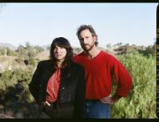 Frau und Mann schräg hintereinanderstehend, beide schauen in die Kamera