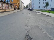 marode Asphalt Straße, links und rechts Wohnblöcke, auf der linken Seite bemalte Wand mit Küchenszenen, auf der rechten Seite Parkplätze entlang der Straße